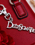 Close-up of Delta Sigma Theta silver Greek letter keychain charm clipped to red handbag with pearl bracelet