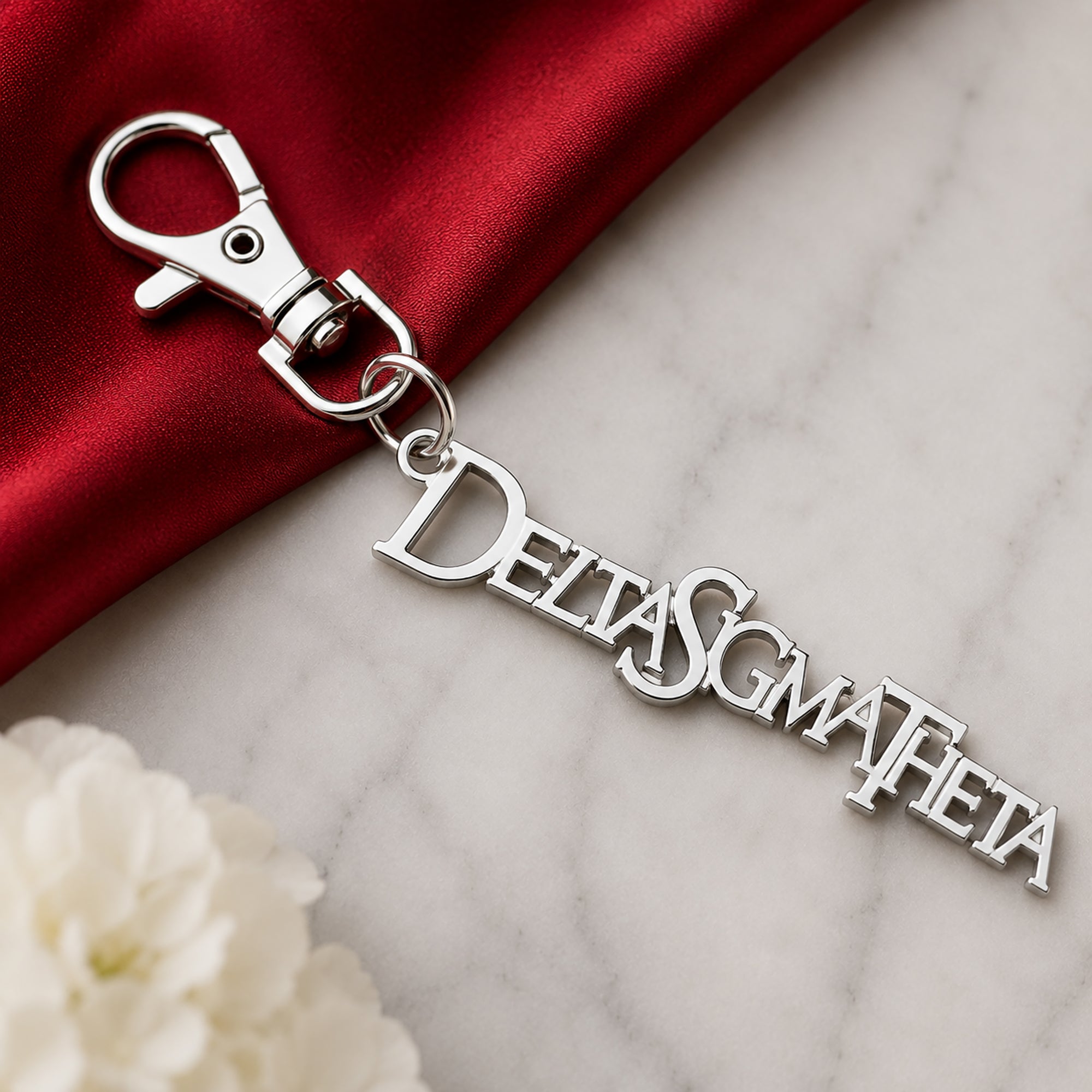 Close-up of Delta Sigma Theta silver Greek letter keychain charm clipped to red handbag with pearl bracelet