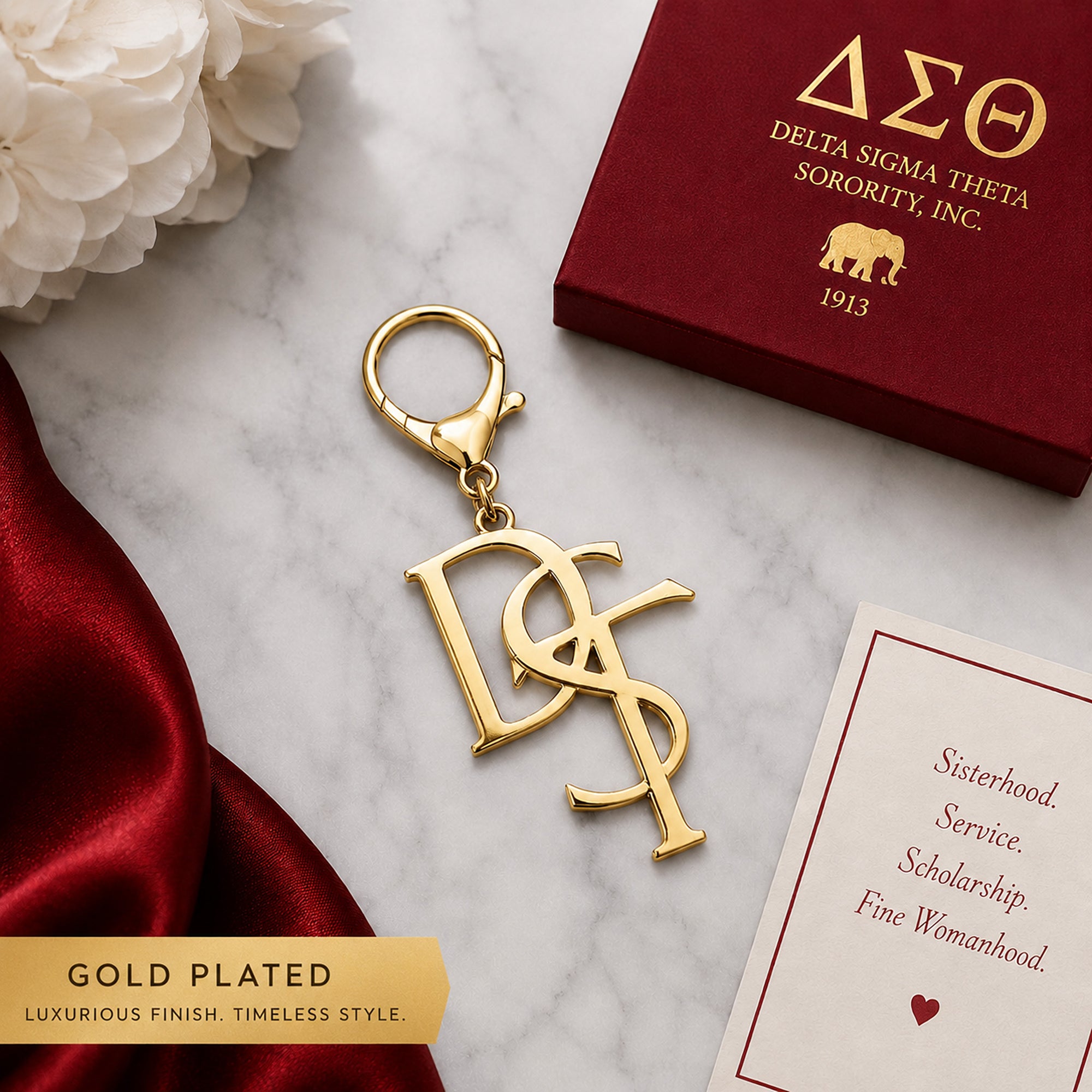 Delta Sigma Theta DST monogram gold keychain with lobster clasp on marble surface next to crimson gift box