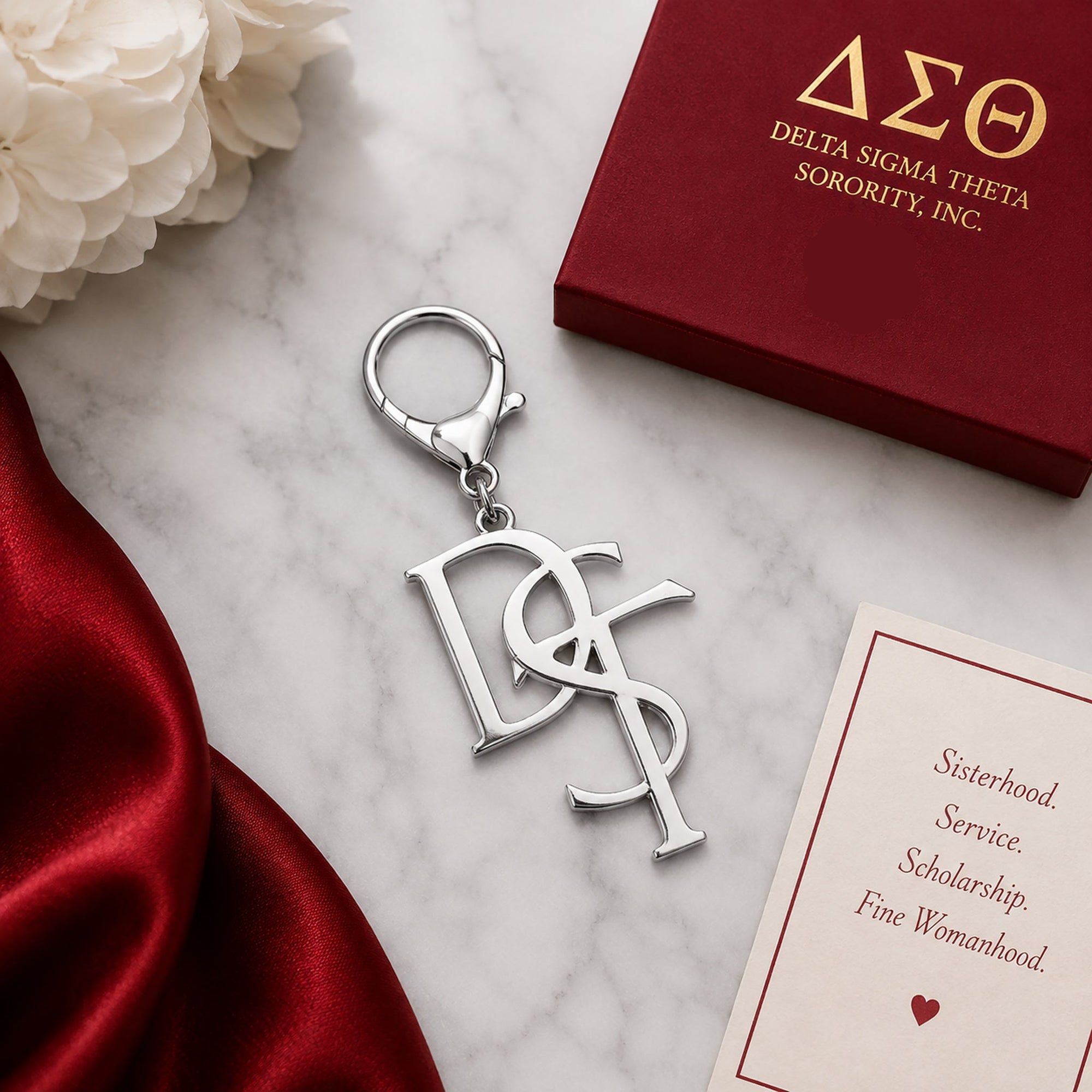 Delta Sigma Theta DST monogram silver keychain with lobster clasp on marble surface next to crimson gift box