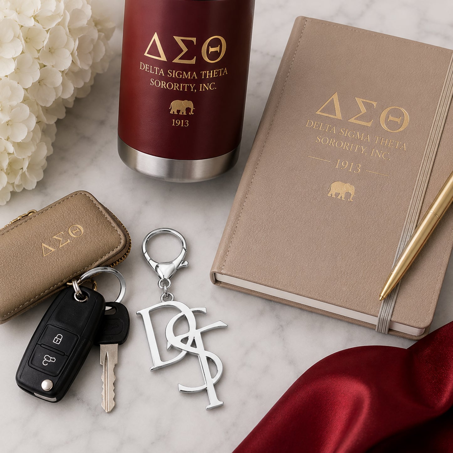 Delta Sigma Theta DST monogram silver keychain styled with car keys, crimson tumbler, and DST journal on marble surface