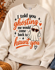 An off-white crewneck sweatshirt with a Halloween graphic print, styled in a cozy autumn setting with a knit blanket, a candle, and denim jeans.