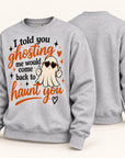 A light heather gray crewneck sweatshirt shown from both front and back. The front features a graphic of a cartoon ghost wearing heart-shaped sunglasses and making a peace sign, surrounded by the text 'I told you ghosting me would come back to haunt you' in black and orange lettering.