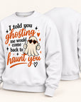 A white crewneck sweatshirt shown from both front and back. The front features a graphic design with the text 'I told you ghosting me would come back to haunt you' in black and orange lettering, alongside a cartoon ghost wearing heart-shaped sunglasses and making a peace sign.