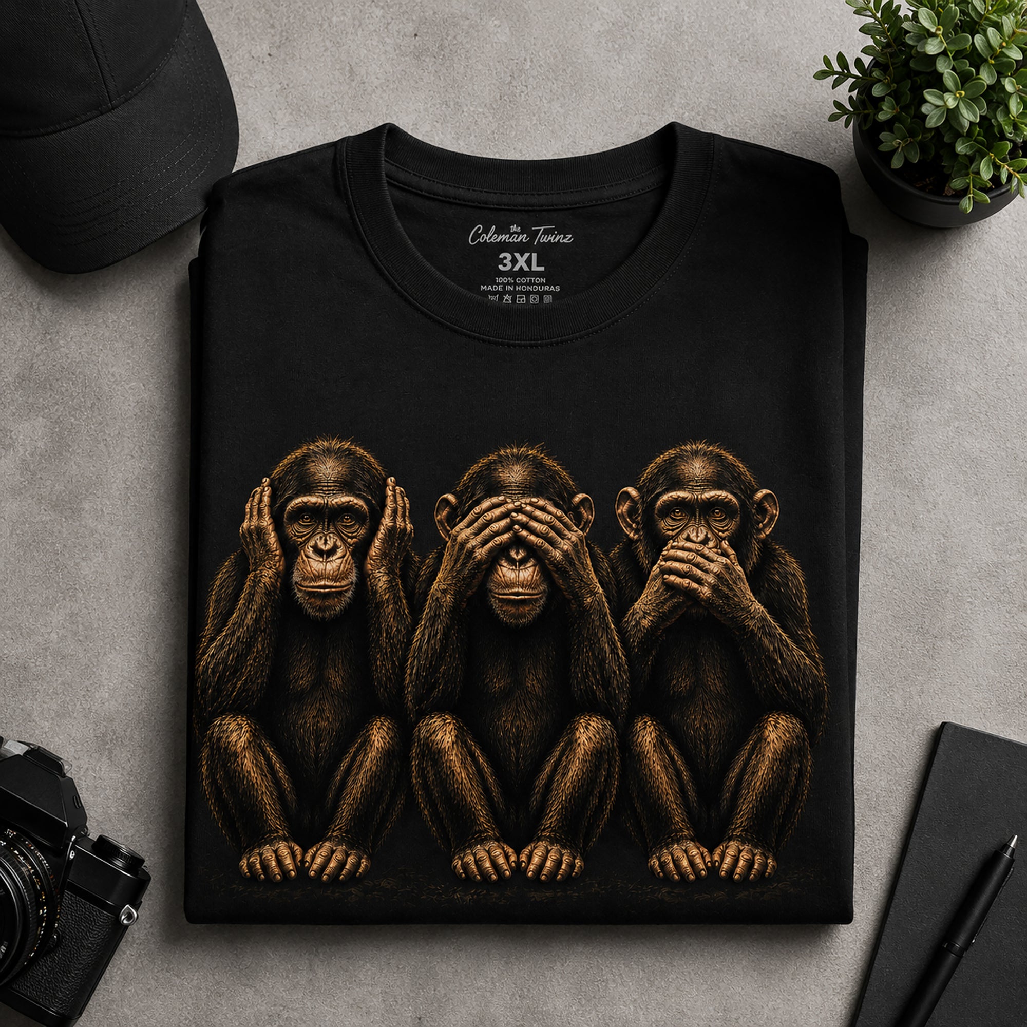 Folded black graphic t-shirt with detailed three wise monkeys artwork displayed in flat lay setup
