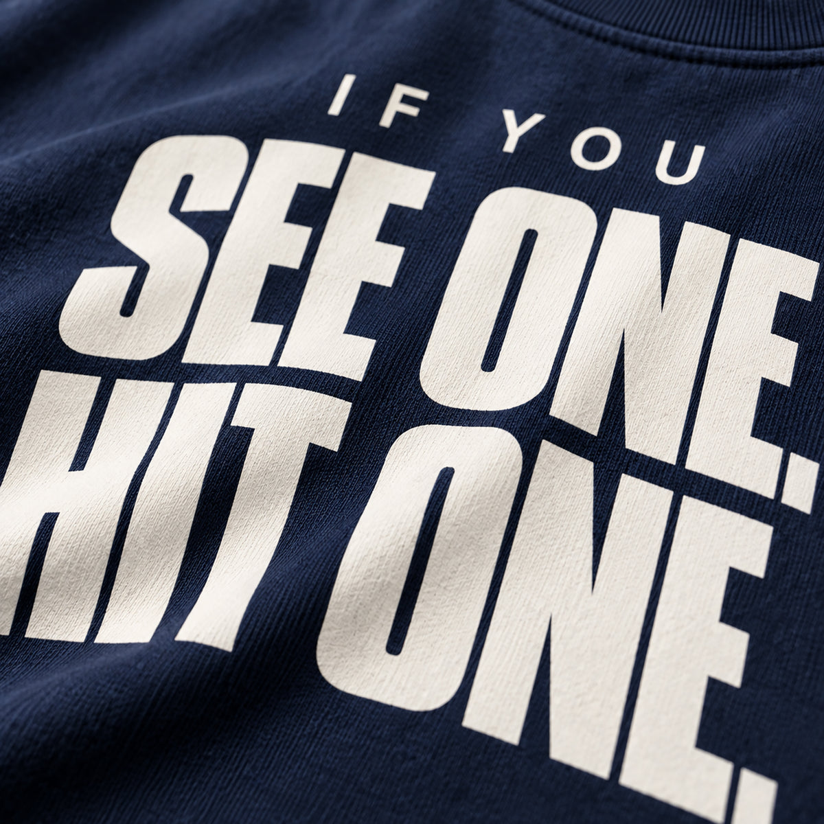Close-up of a navy blue sweatshirt featuring bold white text that reads 'IF YOU SEE ONE, HIT ONE.'
