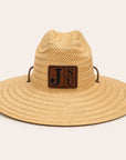 A woven straw safari-style hat in a light tan color, featuring a brown leather patch on the front with the letters 'J', 'S', and 'U' in black, and two small brown side loops.