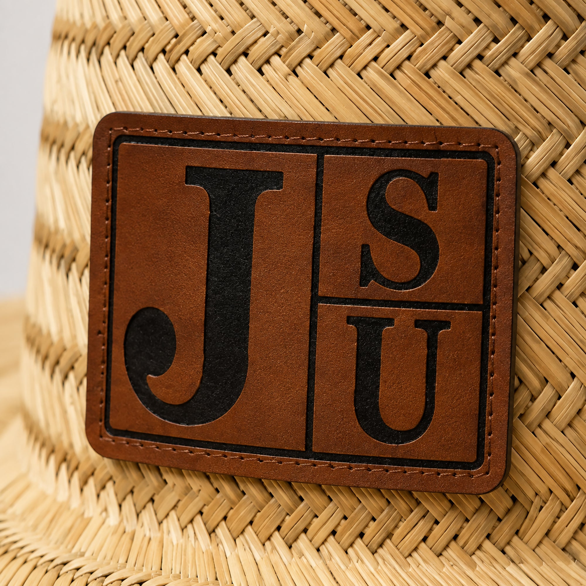 Close-up of walnut and black engraved JSU leatherette patch on Jackson State straw lifeguard hat