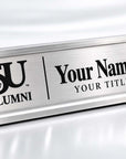 A brushed stainless steel tabletop nameplate with black engraved text reading 'JSU ALUMNI' and 'Your Name Here / YOUR TITLE HERE', shown on a clean white reflective surface.