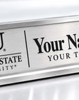 A silver metal desk nameplate with a brushed finish, featuring the Jackson State University logo on the left and customizable text reading 'Your Name Here' and 'YOUR TITLE HERE' on the right.