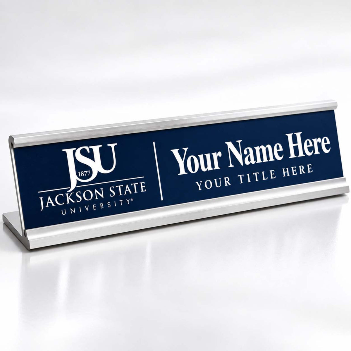 A rectangular desk nameplate with a silver metal frame and a dark blue front panel. The left side shows the white Jackson State University logo and text, while the right side has placeholder text reading 'Your Name Here' and 'YOUR TITLE HERE'.