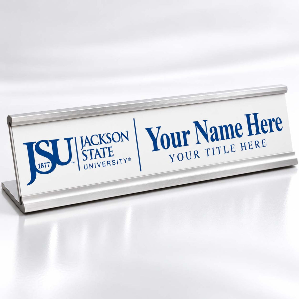 A silver aluminum desk nameplate with a white front panel, featuring the blue Jackson State University logo and customizable text reading 'Your Name Here' and 'Your Title Here'.