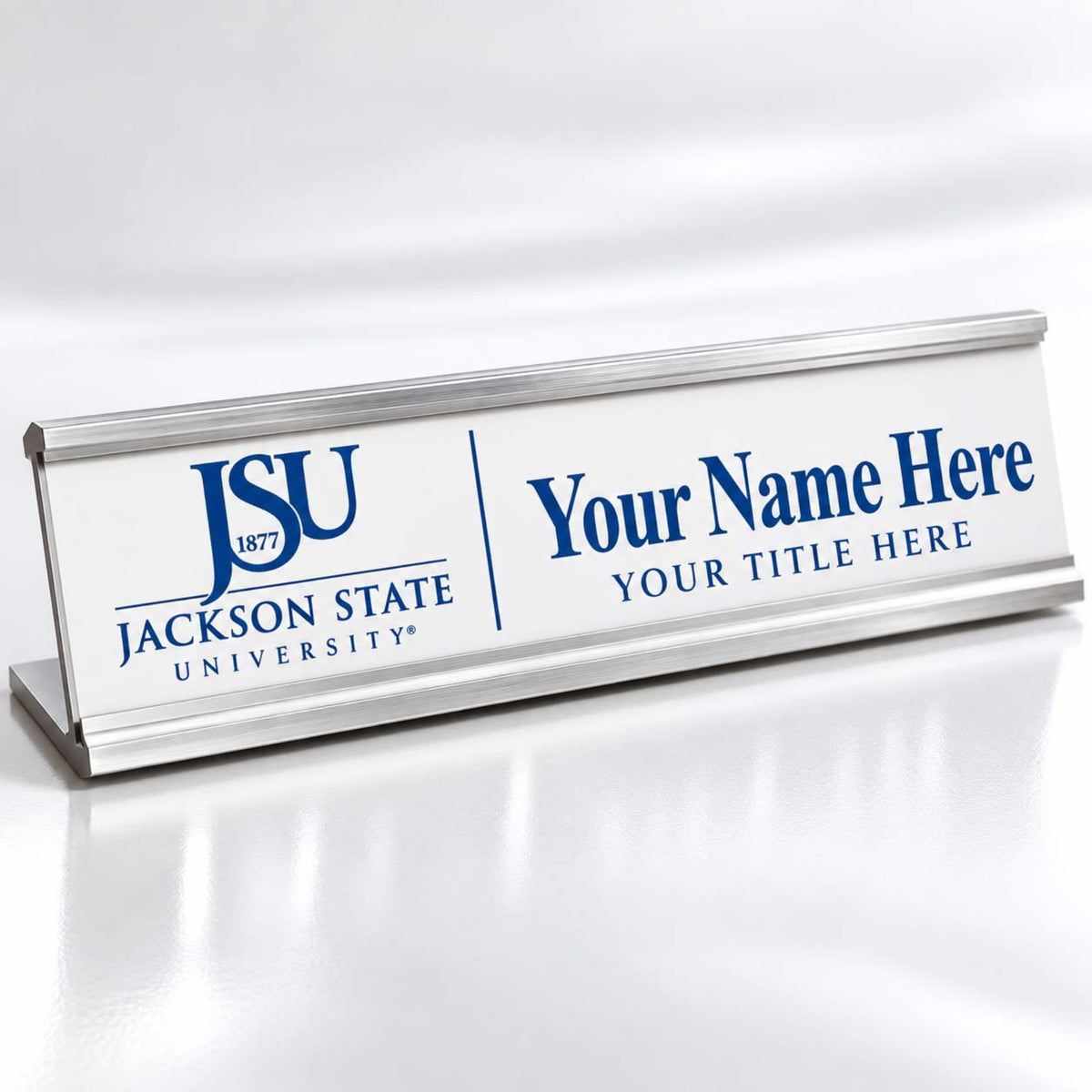 A silver metal desk nameplate with a white front panel, featuring the blue 'JSU Jackson State University' logo on the left and customizable blue placeholder text on the right, shown on a reflective white surface.