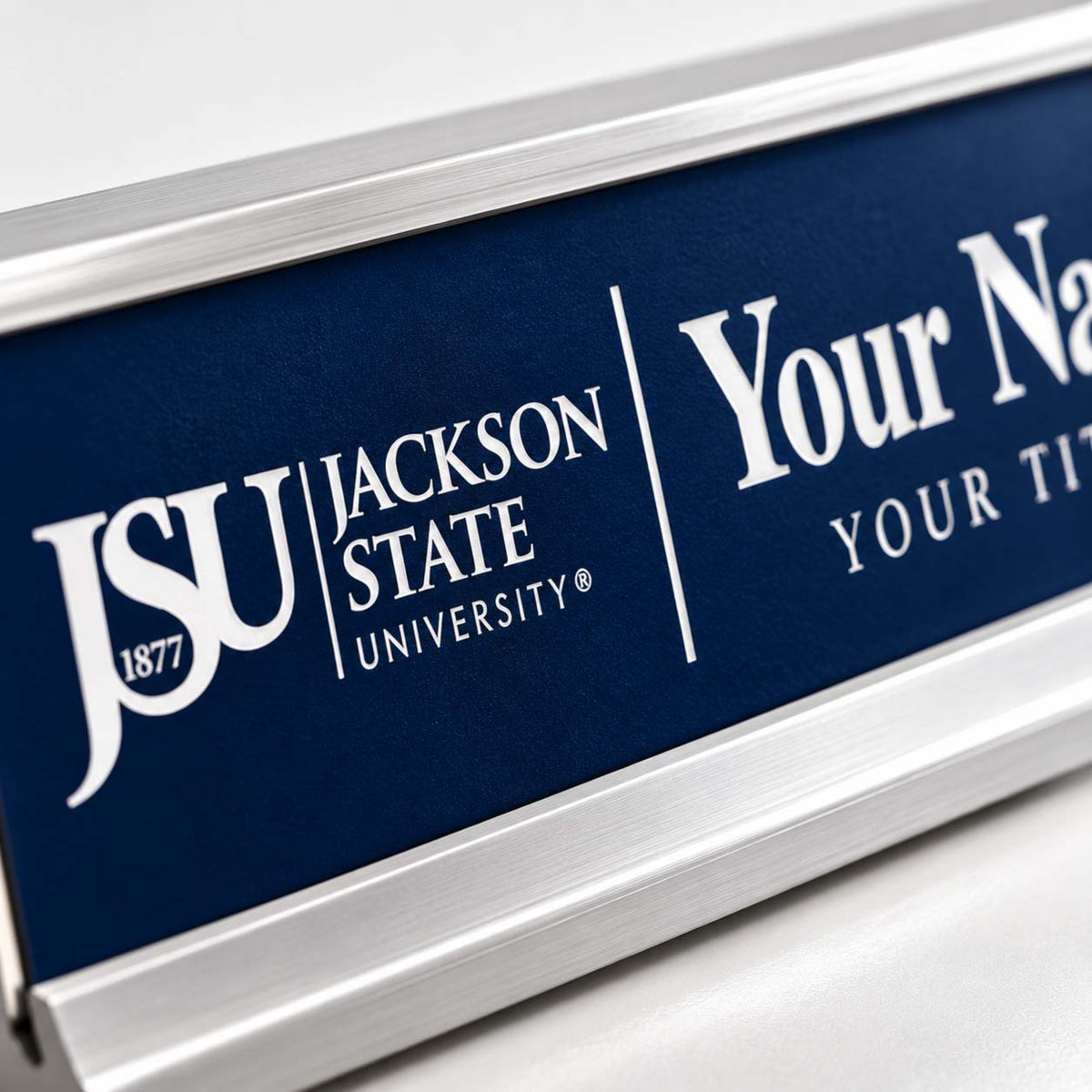 A close-up of a custom nameplate with a dark navy blue background and silver metal frame. The plate features the white text 'JSU JACKSON STATE UNIVERSITY' and placeholder text 'Your Na YOUR TI'.