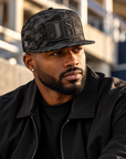 Black man wearing Jackson State Black Camo New Era 9FIFTY flat bill snapback with tone-on-tone black Block JSU leatherette patch
