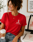 Woman wearing bright red Junior League Women Who Build Essential Tee styled with denim and leadership accessories