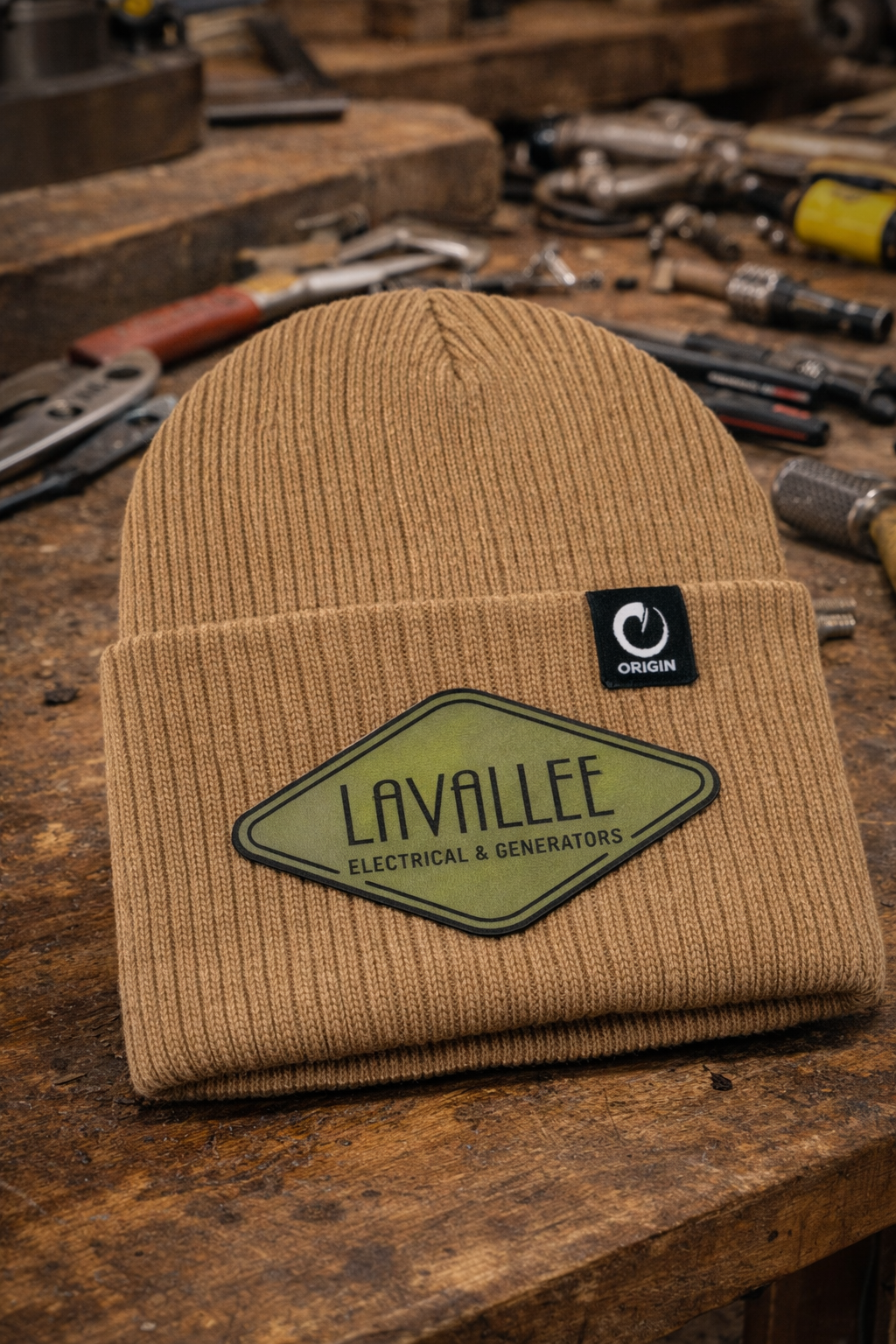Custom Lavallee Electrical & Generators beanie featuring leatherette logo patches in olive green shown on a workbench for electricians and generator technicians.