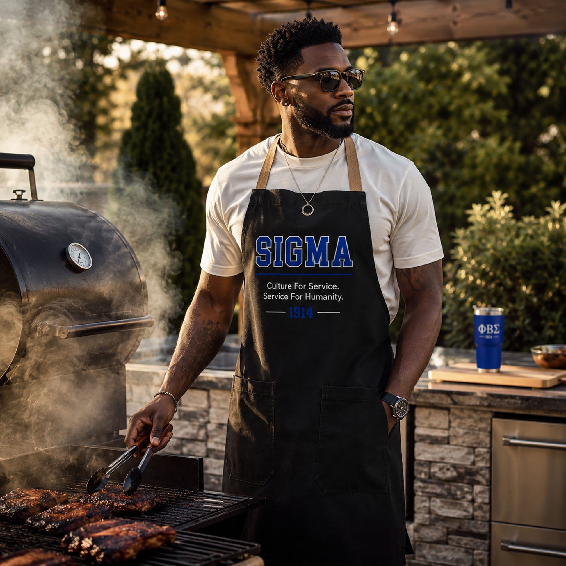Sigma fraternity brother wearing a black grilling apron while cooking outdoors at a barbecue with a smoker