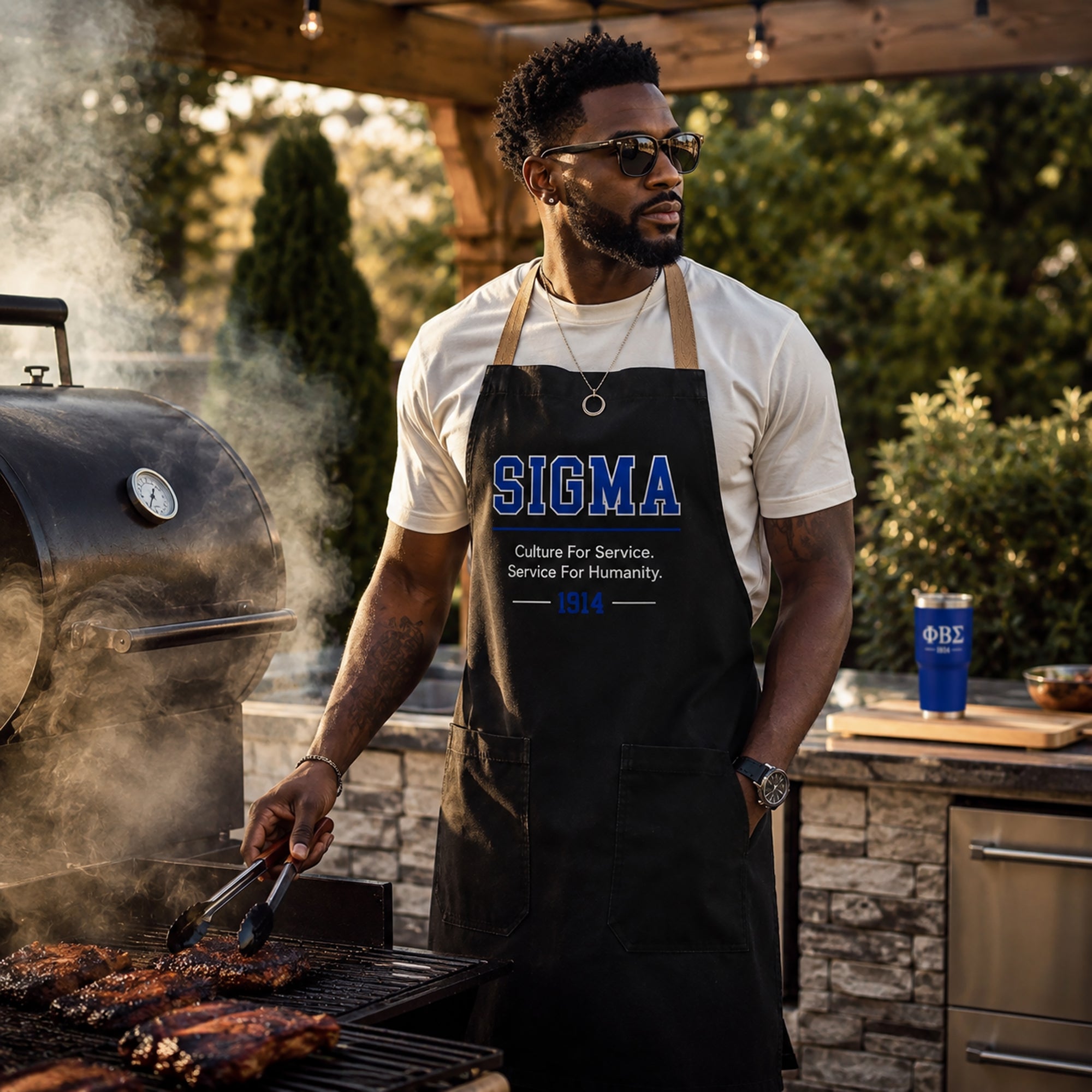 Sigma fraternity brother wearing a black grilling apron while cooking outdoors at a barbecue with a smoker