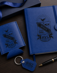 Blue leather notebook with embossed design, keychain, and pen on a dark surface