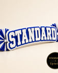 Standard personalized acrylic name spirit stick from the Classic Collection featuring white, royal blue, and white three-layer acrylic with coordinating royal blue and white pom-poms, available up to 16 inches.