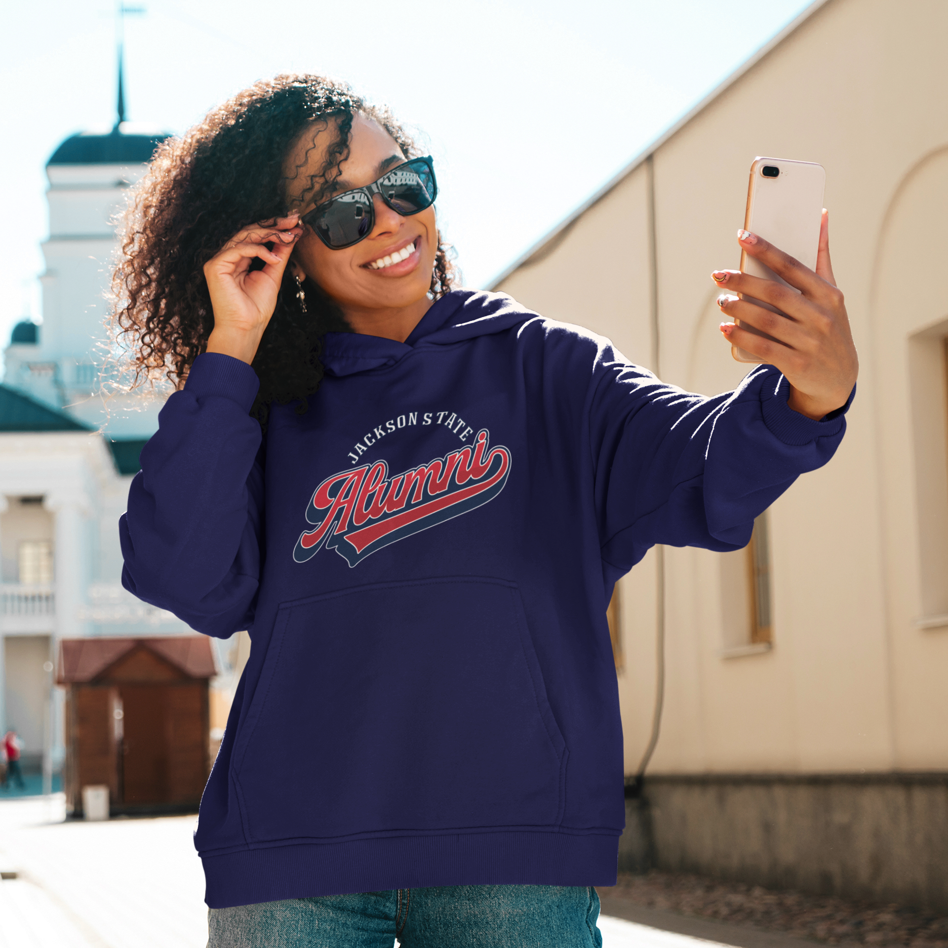 Navy pullover hoodie with Alumni logo on chest, worn by a smiling woman outdoors